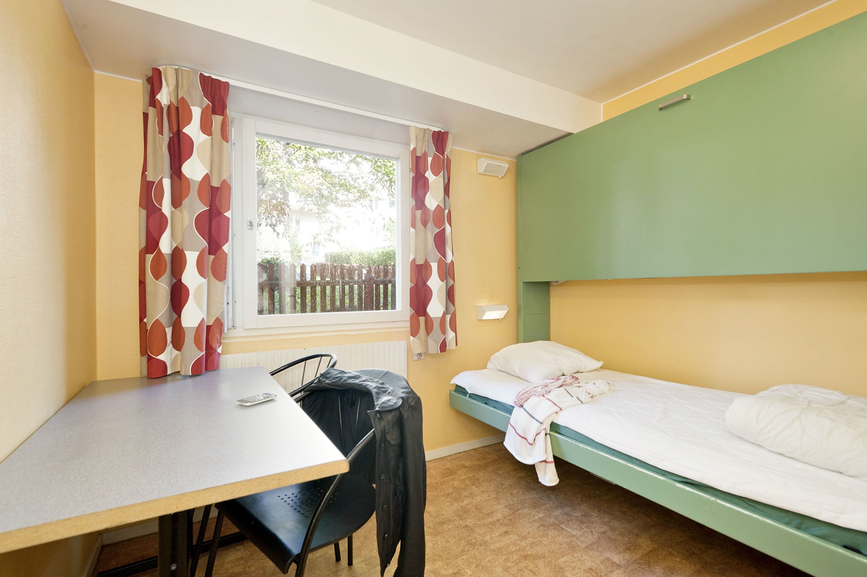 Una piccola stanza singola con un letto, una scrivania e una sedia.