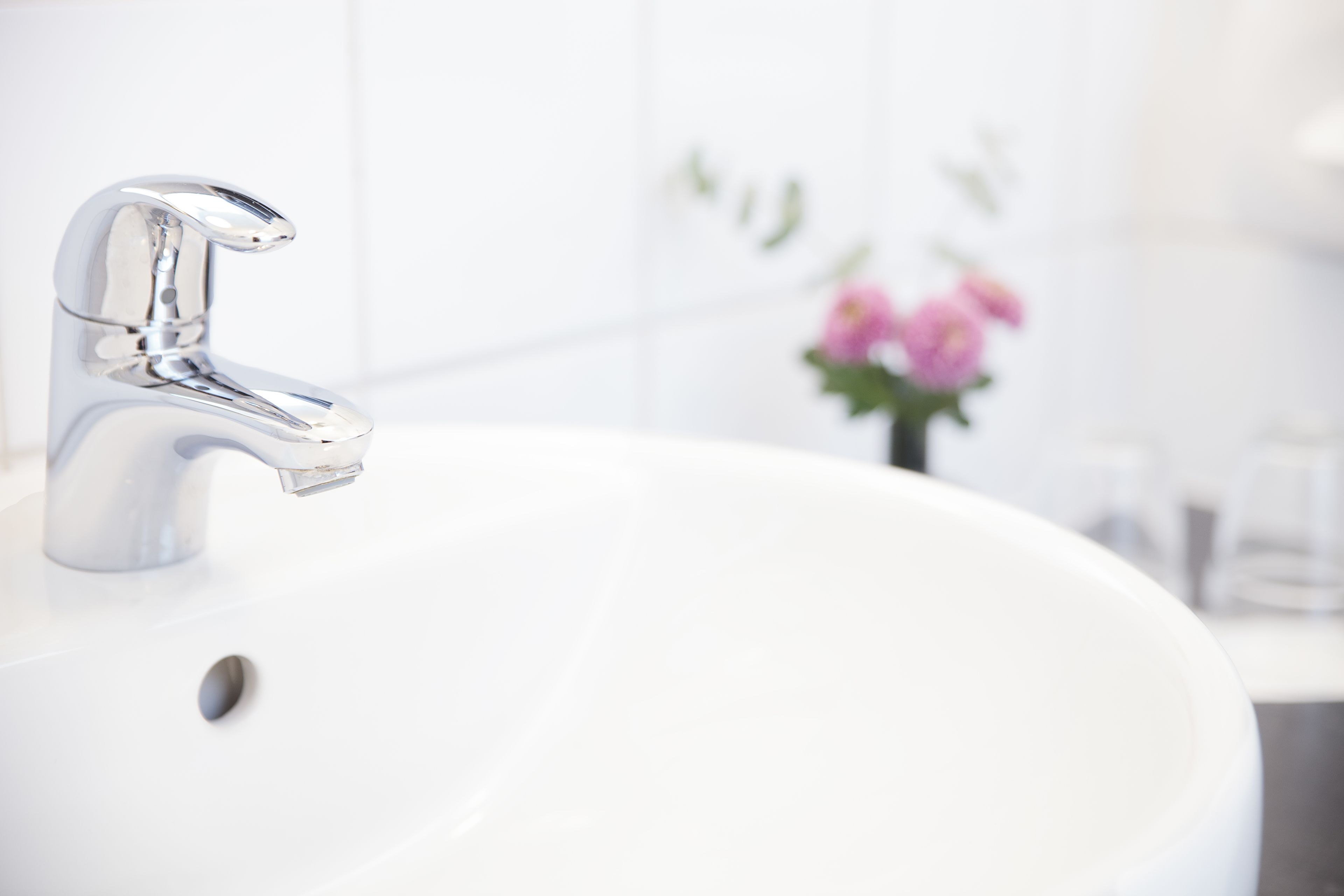 Un lavamanos moderno con grifo cromado, un lavabo blanco y un pequeño arreglo floral al fondo.