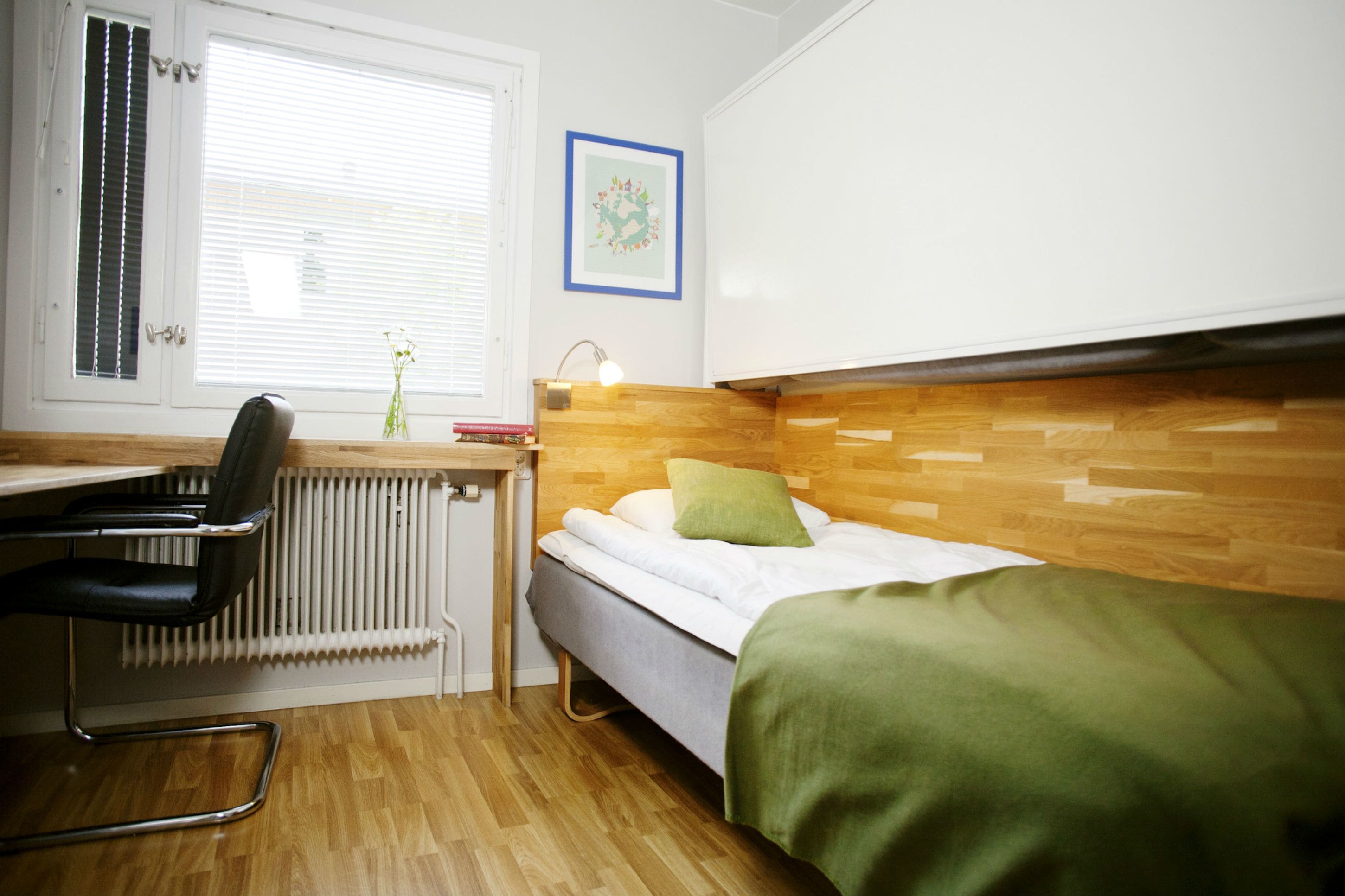 A compact room with a bed, a desk, a chair, and a radiator.