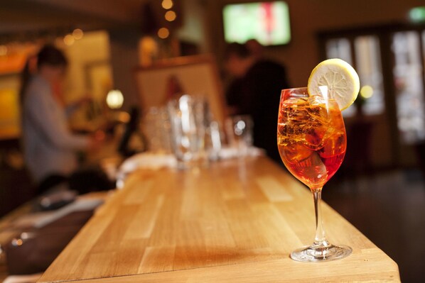 A bar with a wooden counter and a glass of red beverage garnished with a lemon slice. - STF Zinkensdamm Hostel (Stockholm)
