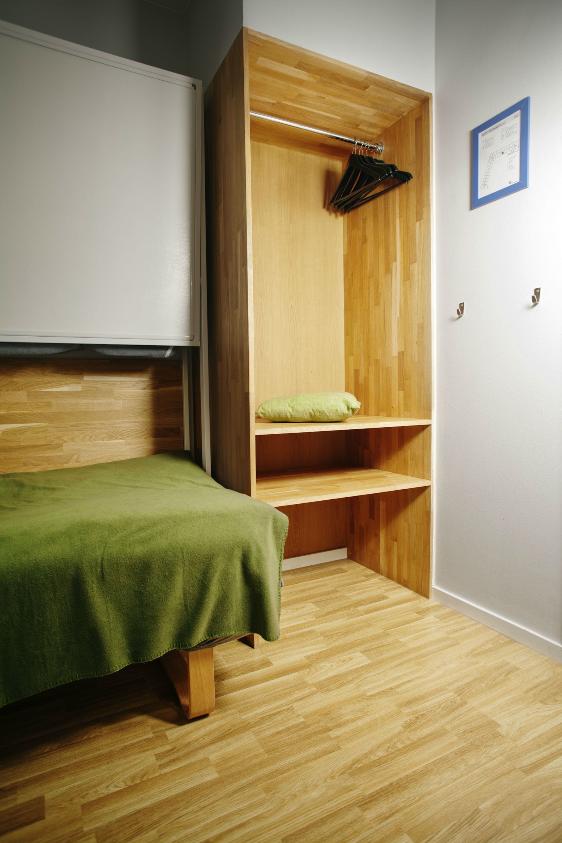 Habitació petita amb un llit, un armari de fusta i una prestatgeria amb una tovallola verda.