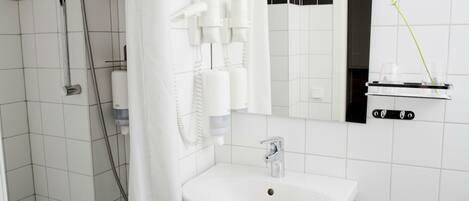 A modern bathroom with a white sink, a shower with a curtain, a mirror, and a light fixture.