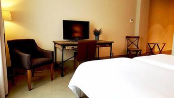 A hotel room with a bed, a desk with a television, a chair, and a small table.