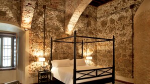 A four-poster bed in a room with stone walls and a wooden floor.