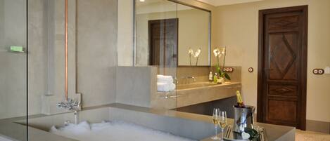 Un baño moderno con una bañera grande, una ducha con mampara de vidrio, un tocador con espejo y una puerta con panel decorativo.