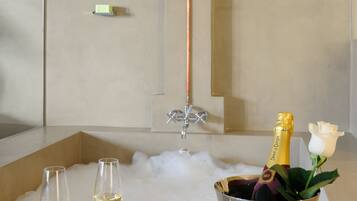 Een moderne badkamer met een douche, een bad vol bubbels en een champagnekoeler met glazen en een roos.