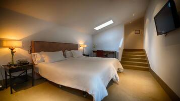 Una habitación de hotel con una cama grande, mesitas de noche, un escritorio, una silla, un televisor fijado a la pared y una escalera que sube a otro nivel.