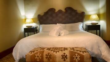 A neatly made bed with white linens and two rolled towels, a patterned ottoman, and two bedside lamps on nightstands.