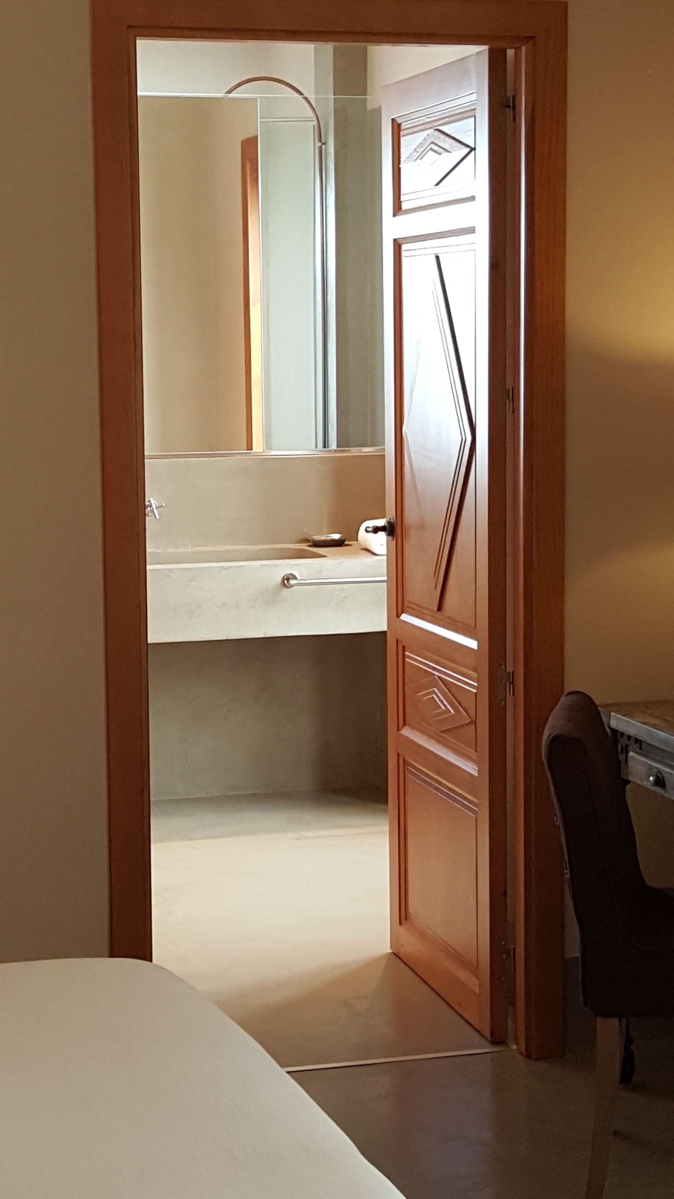 A narrow hallway leading to a bathroom with a mirror, sink, and towel rack.