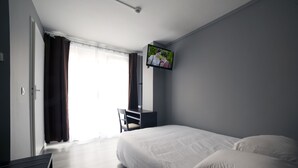 A hotel room with a bed, a desk, a chair, and a television on the wall. - Citadel Hotel (Calais)