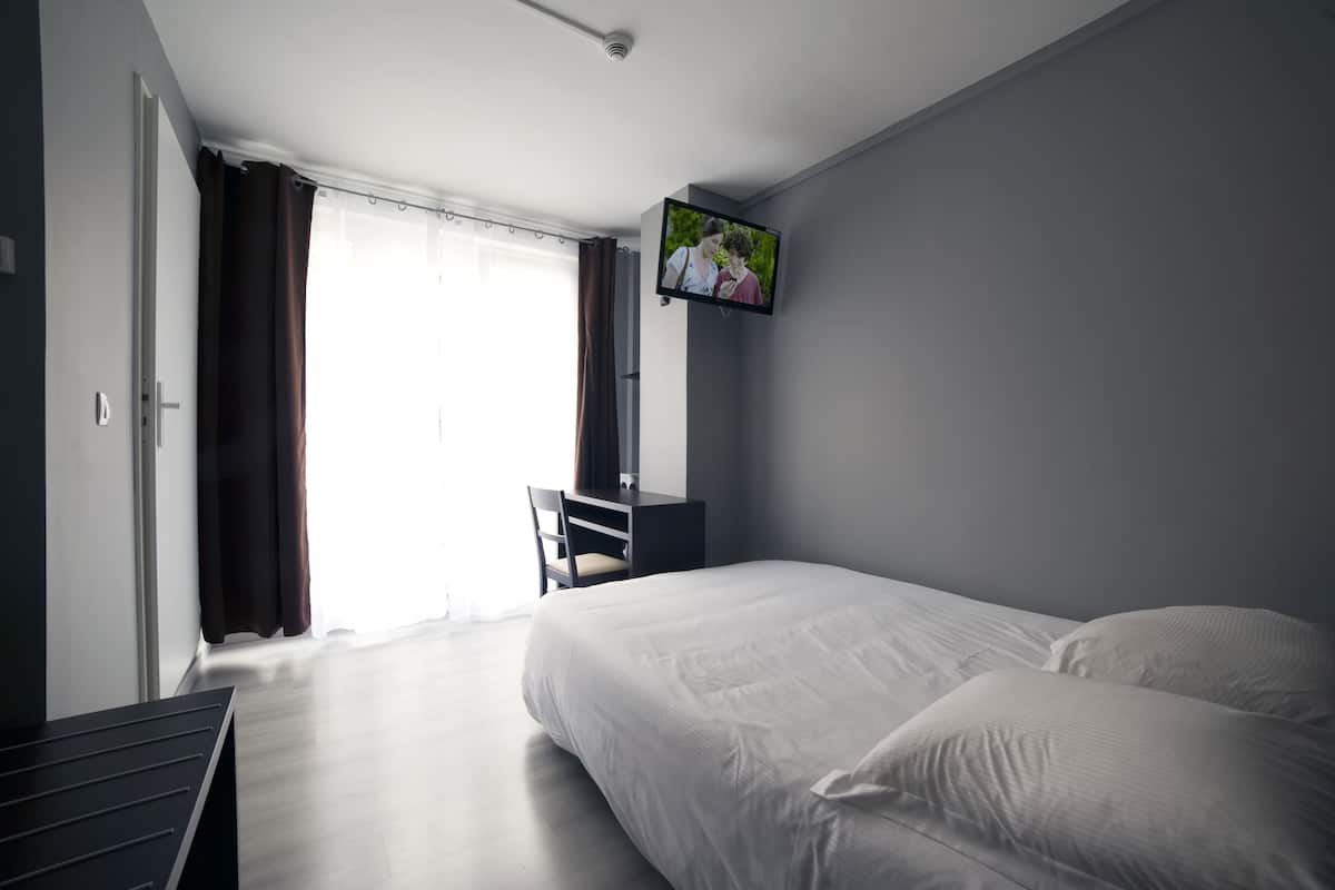 A hotel room with a bed, a desk, a chair, and a television on the wall.