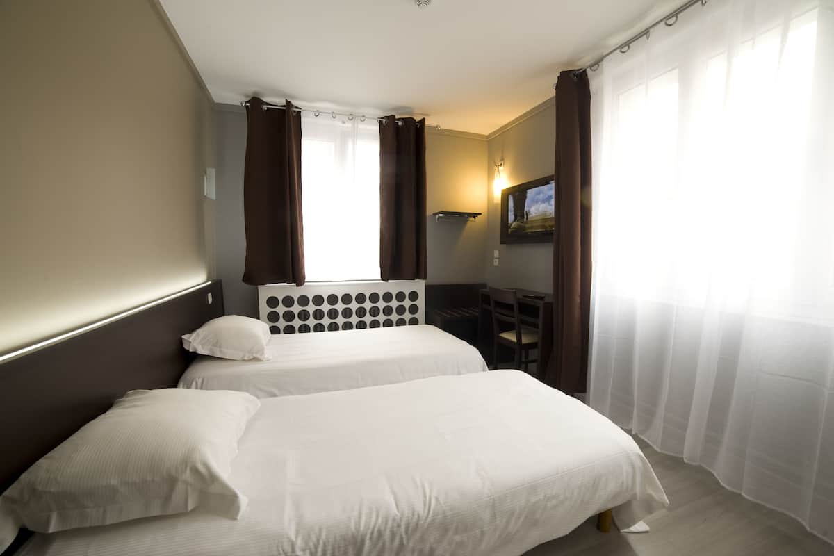 A hotel room with two beds, a desk, a chair, a lamp, and a painting on the wall.