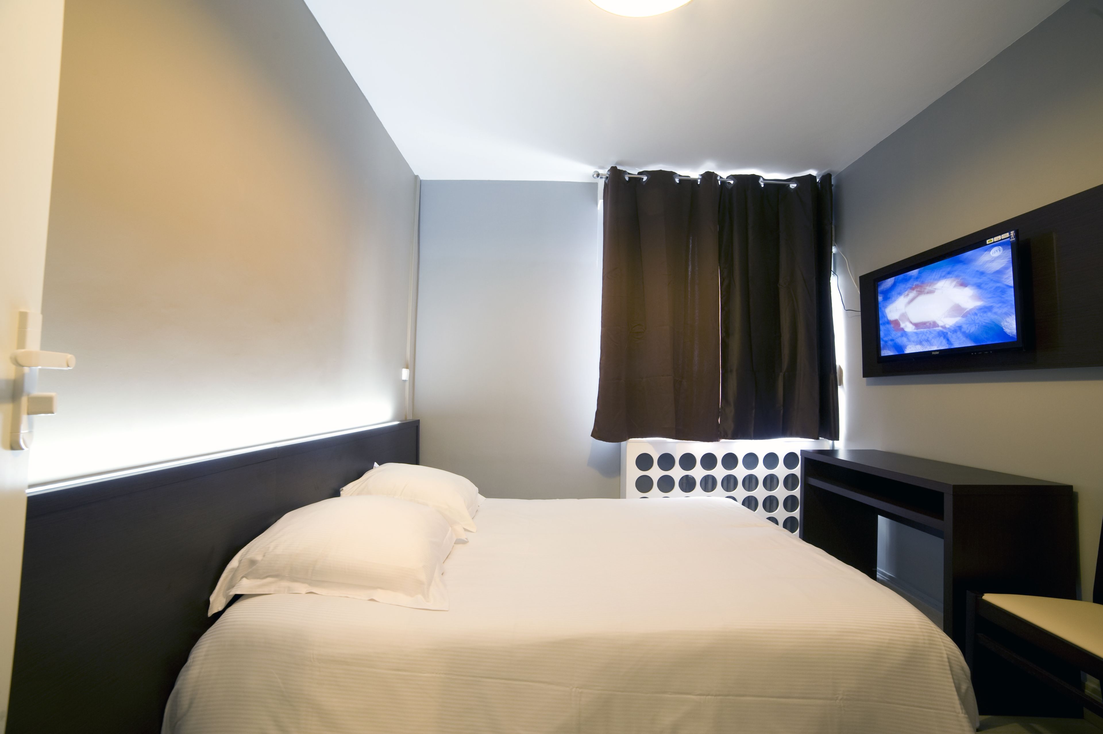 A hotel room with a bed, a TV mounted on the wall, and a window with curtains.