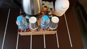 A kitchen counter with a coffee maker, four water bottles, a paper cup, and a tray with coffee beans. - Citadel Hotel (Calais)