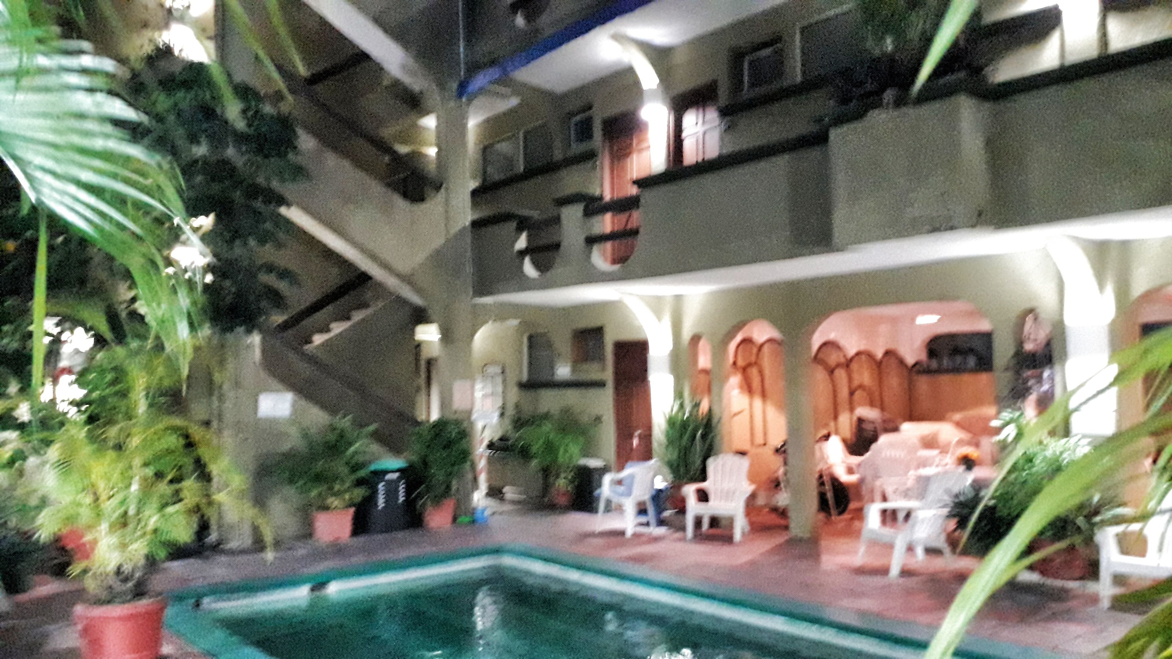 Un espacio interior de varios niveles con una piscina central, zonas de estar y plantas en macetas.