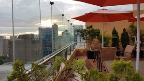 A balcony with outdoor seating, a red umbrella, and a city view. - Apart Hotel San Martin (Lima)