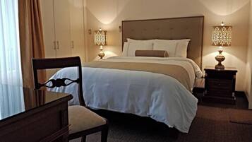 A hotel room with a large bed, a wooden chair, two bedside tables with lamps, and a window with curtains.