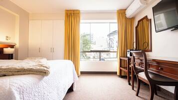 Habitación de hotel con cama, escritorio, silla, televisor y ventana con cortinas.