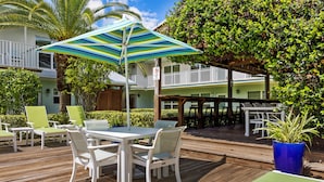 A wooden deck with outdoor seating, a striped umbrella, and a view of a building with balconies. - Sun Dek Beach House (Boynton Beach)