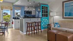 A modern kitchen with a central island, bar stools, and a dining area with a table and chairs. - Sun Dek Beach House (Boynton Beach)