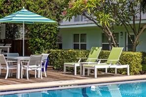 A poolside area with a table and chairs, a striped umbrella, and a pool.