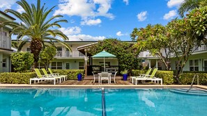 A pool area with lounge chairs, a table, and umbrellas.