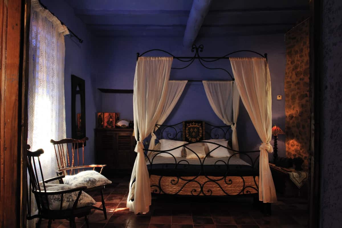A bedroom with a four-poster bed, a chair, and a nightstand.