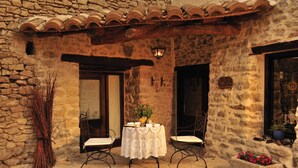 An outdoor seating area with a table and chairs, a stone wall, and a tiled roof.