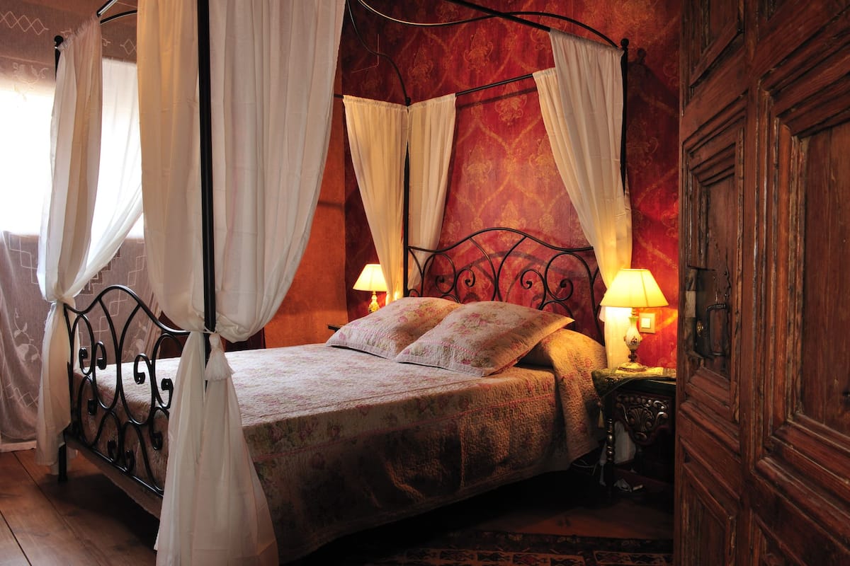 A four-poster bed with white drapes, two bedside lamps, and a wooden wardrobe.