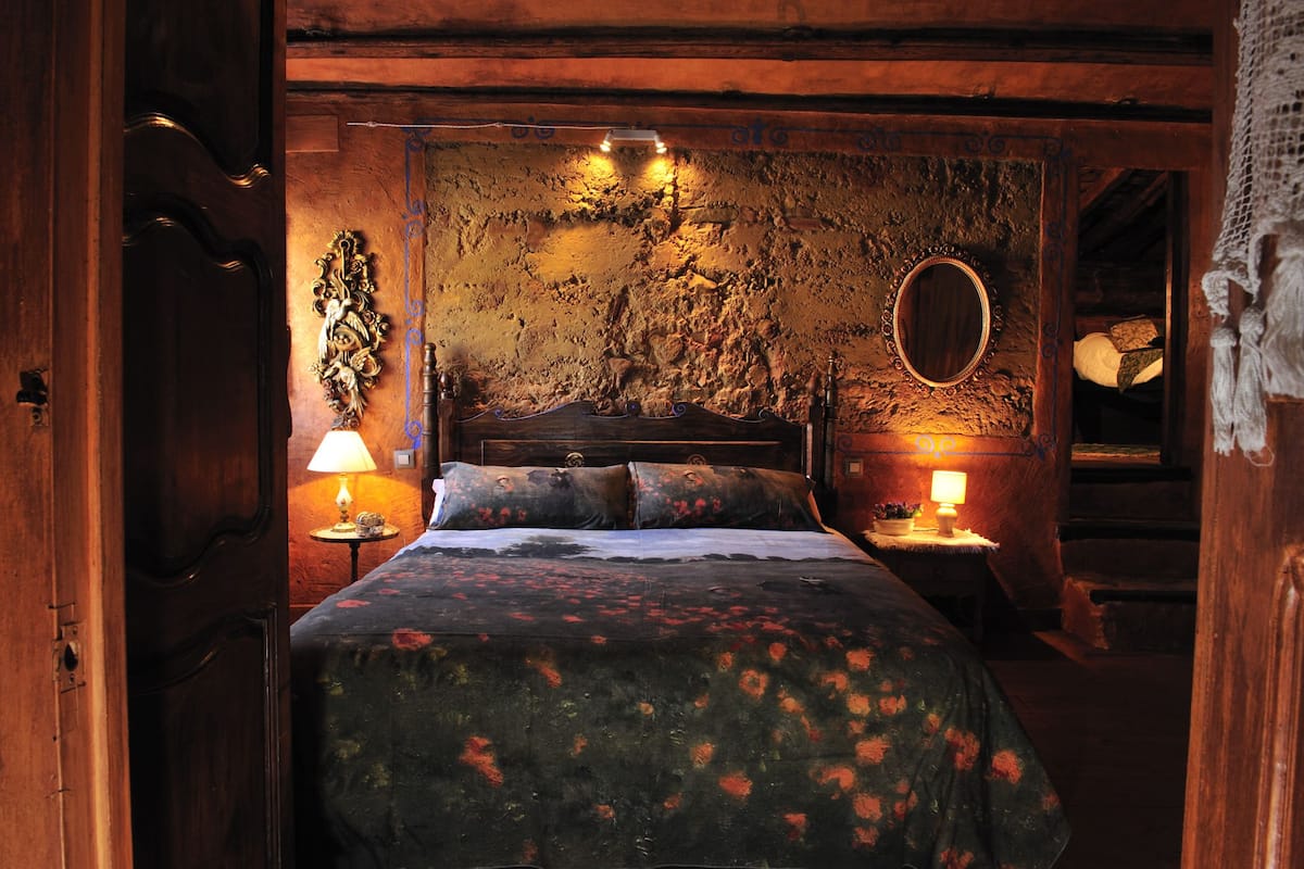 A room with a bed, two bedside lamps, a mirror, and a rustic wall.
