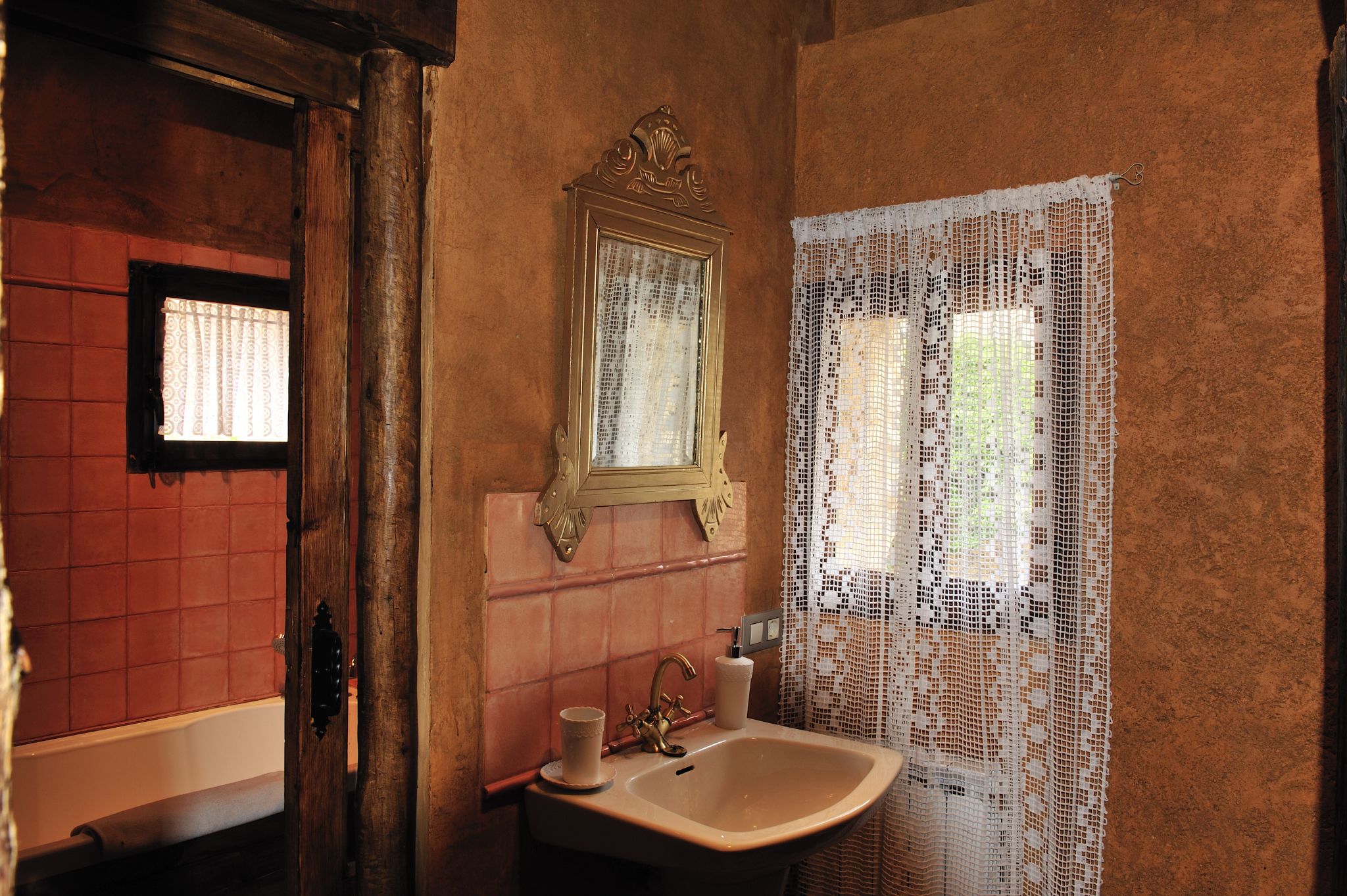 Un baño con lavamanos, espejo y ventana con cortinas de encaje.