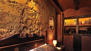 A rustic room with a stone wall, wooden bed, and shelves with books and decorative items.