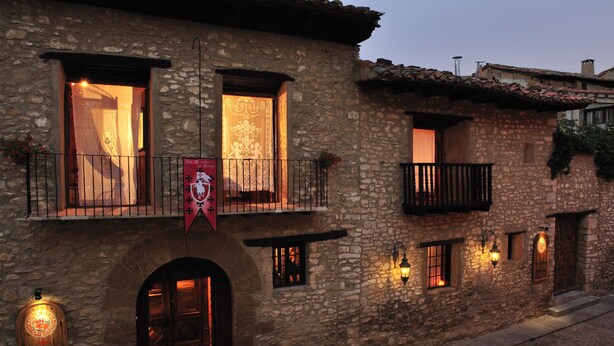 A stone building with multiple windows and balconies, featuring a red banner and a sign indicating it is a hotel.