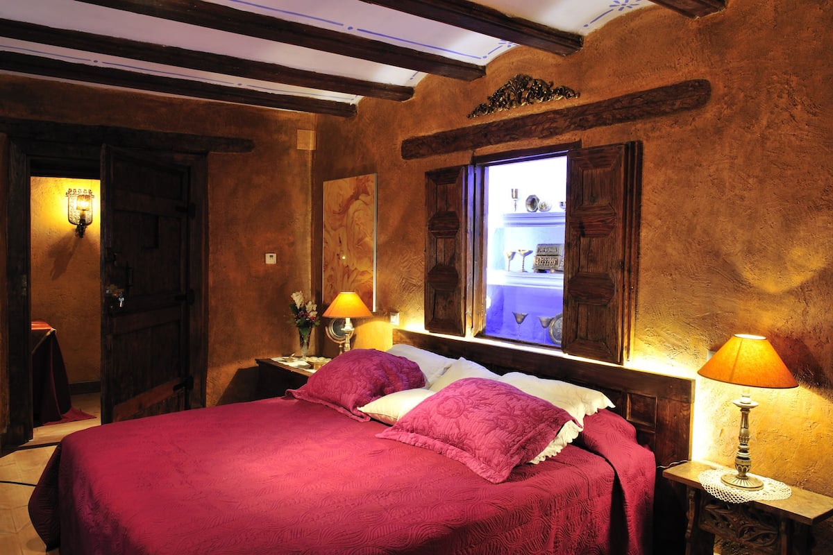 A room with a bed, two nightstands, a window with shutters, and a wooden ceiling.
