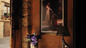 A rustic interior with a stone wall, a framed painting, a vase with flowers, and a lamp.