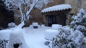 A snow-covered outdoor area with stone walls, a patio with snow-covered furniture, and a tree.