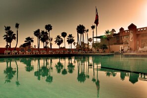 A swimming pool with lounge chairs and palm trees, reflecting in the water. - Hotel Villa Marina (Ensenada)