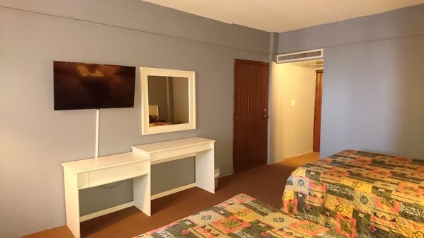 A bedroom with a bed, a desk with a mirror, and a television on the wall. - Hotel Villa Marina (Ensenada)