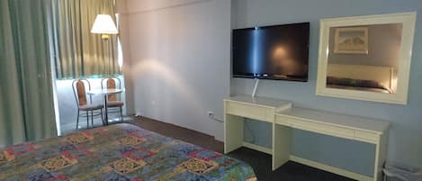 Una habitación de hotel con cama, escritorio con televisor, silla y ventana con cortinas.