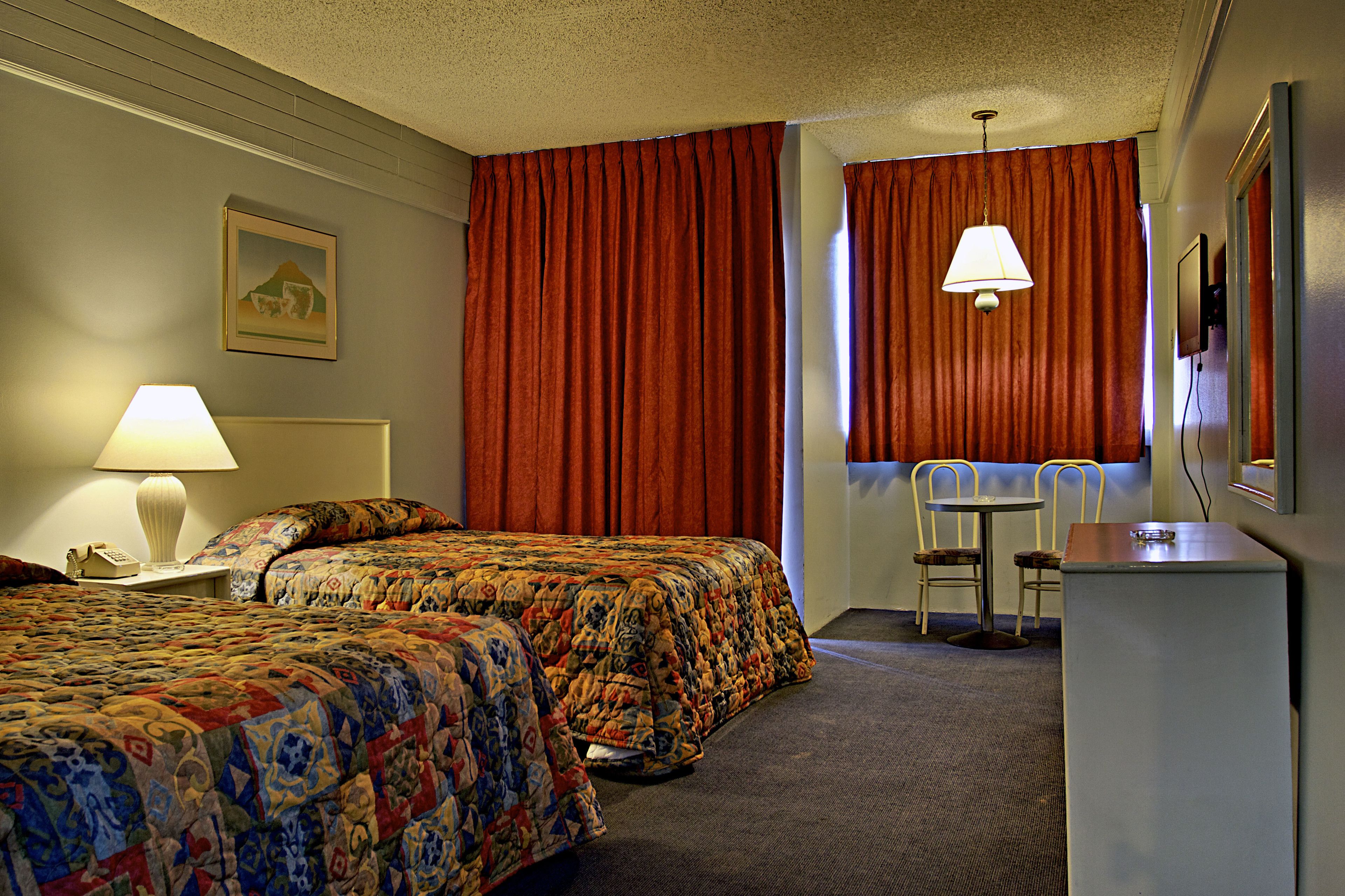 A hotel room with two beds, a desk, a chair, a lamp, and a painting on the wall.