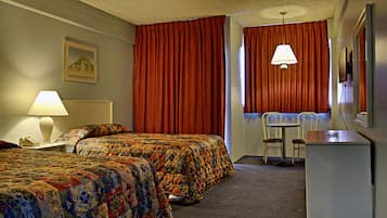 Hotelkamer met twee bedden, een bureau, een stoel, een lamp en een schilderij aan de muur.