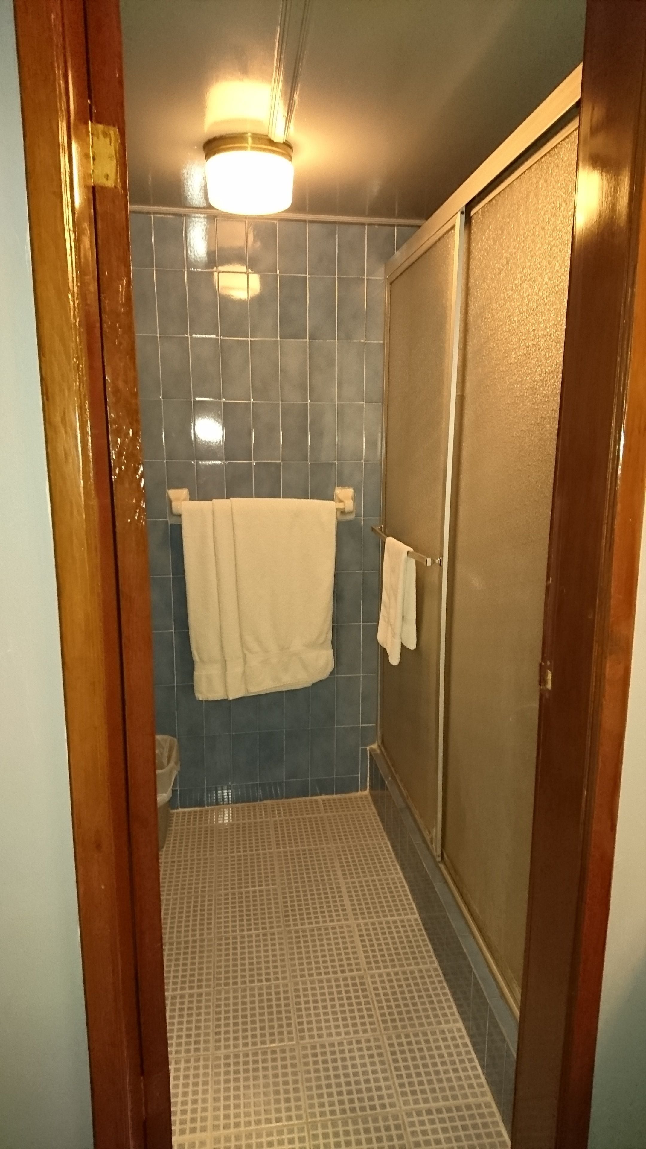 A bathroom with a shower, tiled walls, a visible towel rack, and a door.