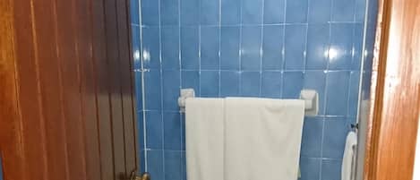 A bathroom with blue tiles, a white towel hanging on a rack, and a wooden door.