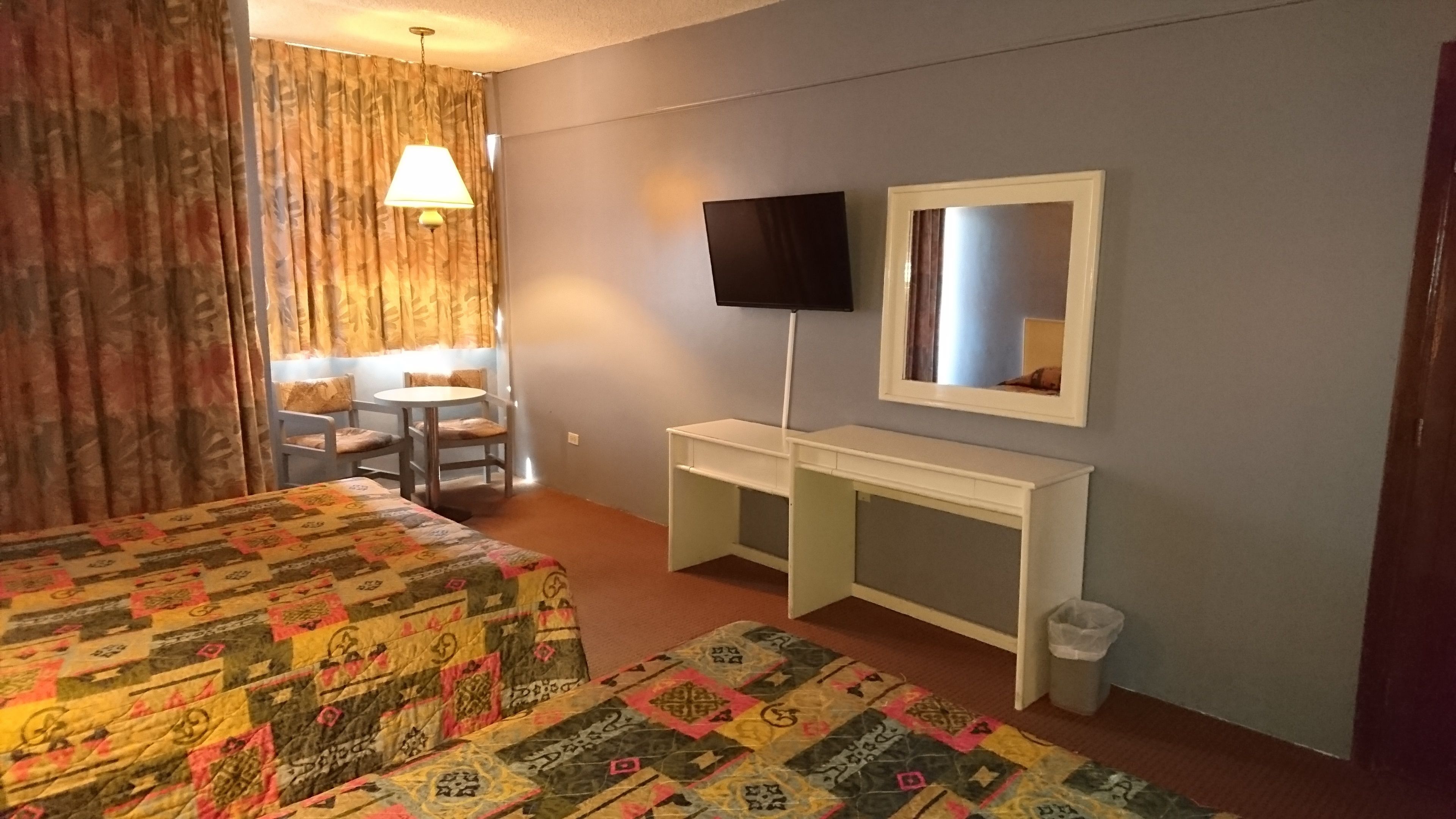 Ett hotellrum med två sängar, ett skrivbord, en TV och ett fönster med gardiner.