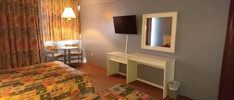 Ett hotellrum med två sängar, ett skrivbord, en TV och ett fönster med gardiner.