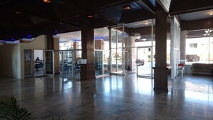 A spacious lobby with a glass door entrance, a reception desk, and a seating area with tables and chairs.