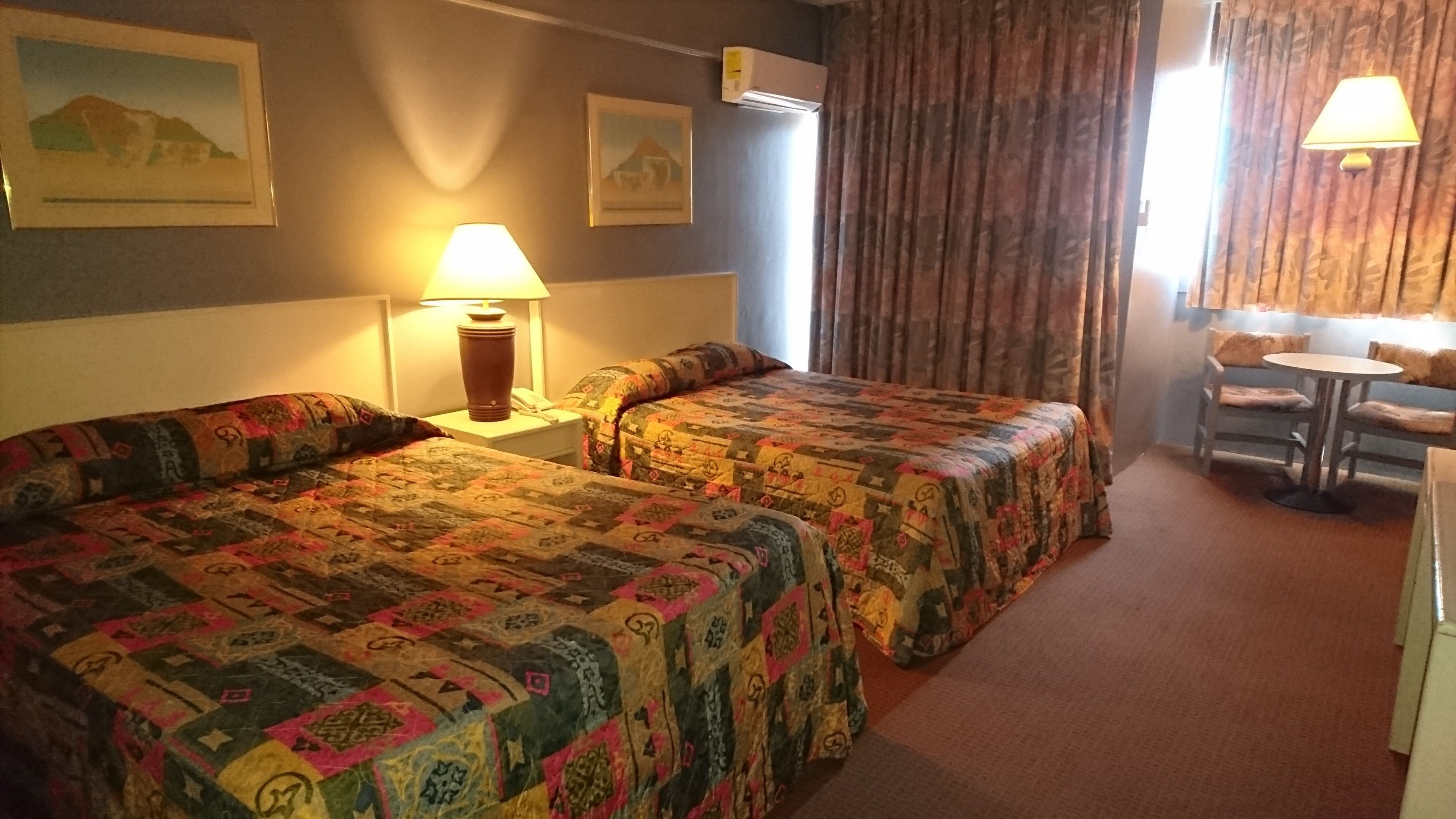 A hotel room with two beds, a small table, and a chair.