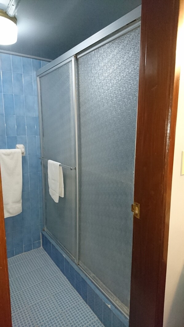 A bathroom with a shower area, blue tiles, and a white towel hanging on a rack. - Hotel Villa Marina (Ensenada)