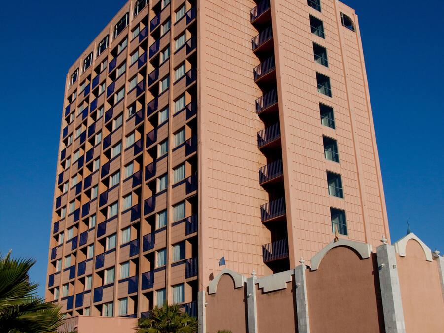 A tall hotel with a distinctive pink facade and a sign in a foreign script.