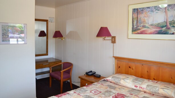 A hotel room with a bed, a desk, a chair, a telephone, and a painting on the wall. - Maples Motel (Orillia)